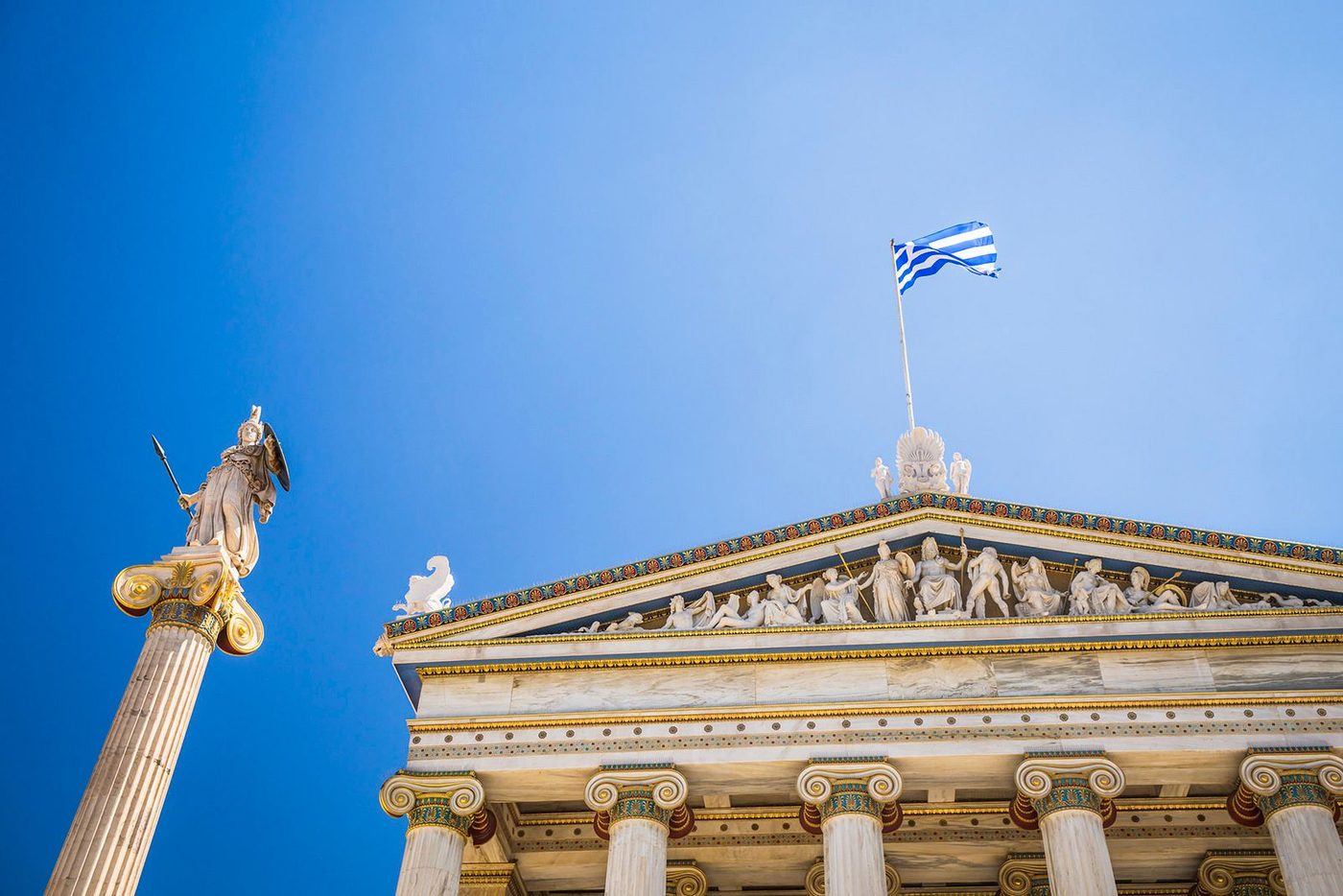The Academy of Athens with a statue of Athena and the Greek flag against a blue sky