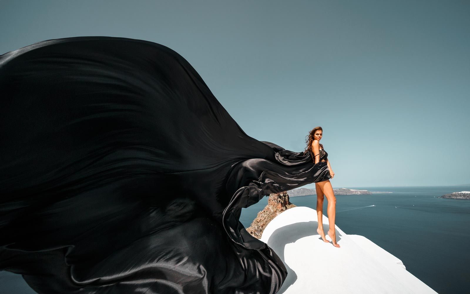 Woman in a black flying dress on a white rooftop above the sea
