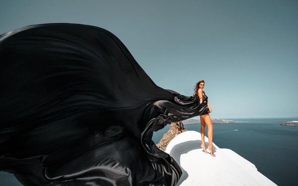 Woman in a black flying dress on a white rooftop above the sea