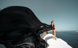 Woman in a black flying dress on a white rooftop above the sea