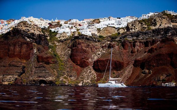 Catamaran anchored beneath a whitewashed village on the red caldera cliffs