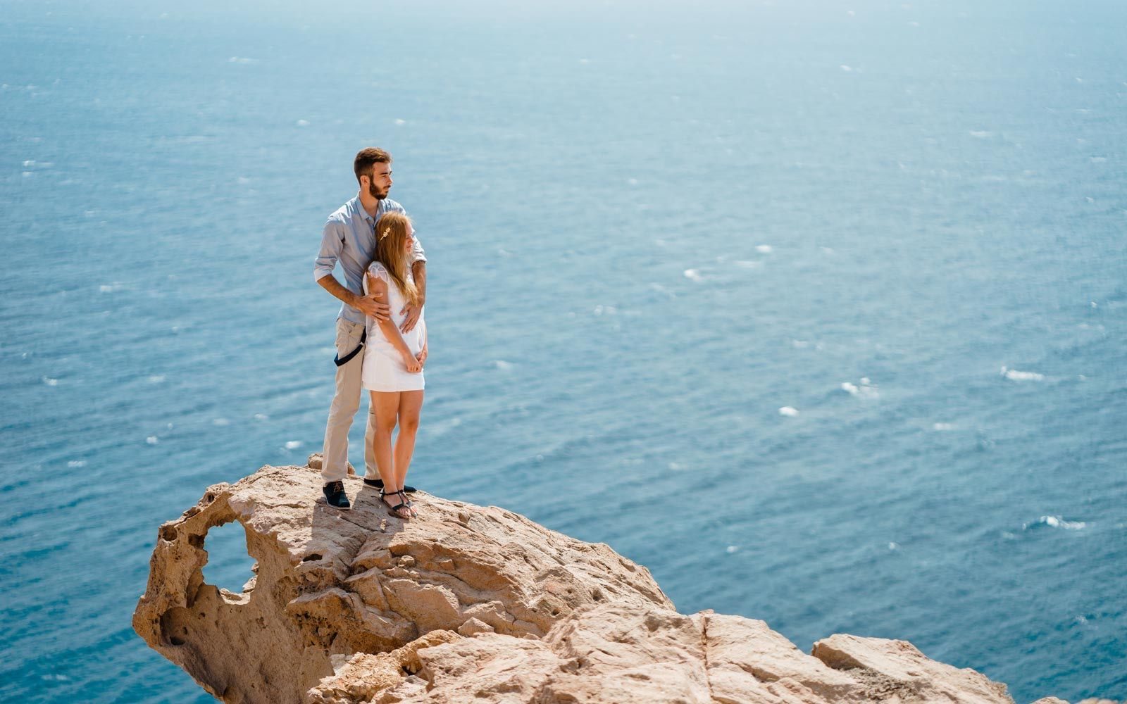 Couple embracing on the edge of a sea cliff above deep blue water