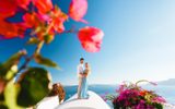Couple embracing on a whitewashed rooftop in Imerovigli, bougainvillea and caldera sea around them