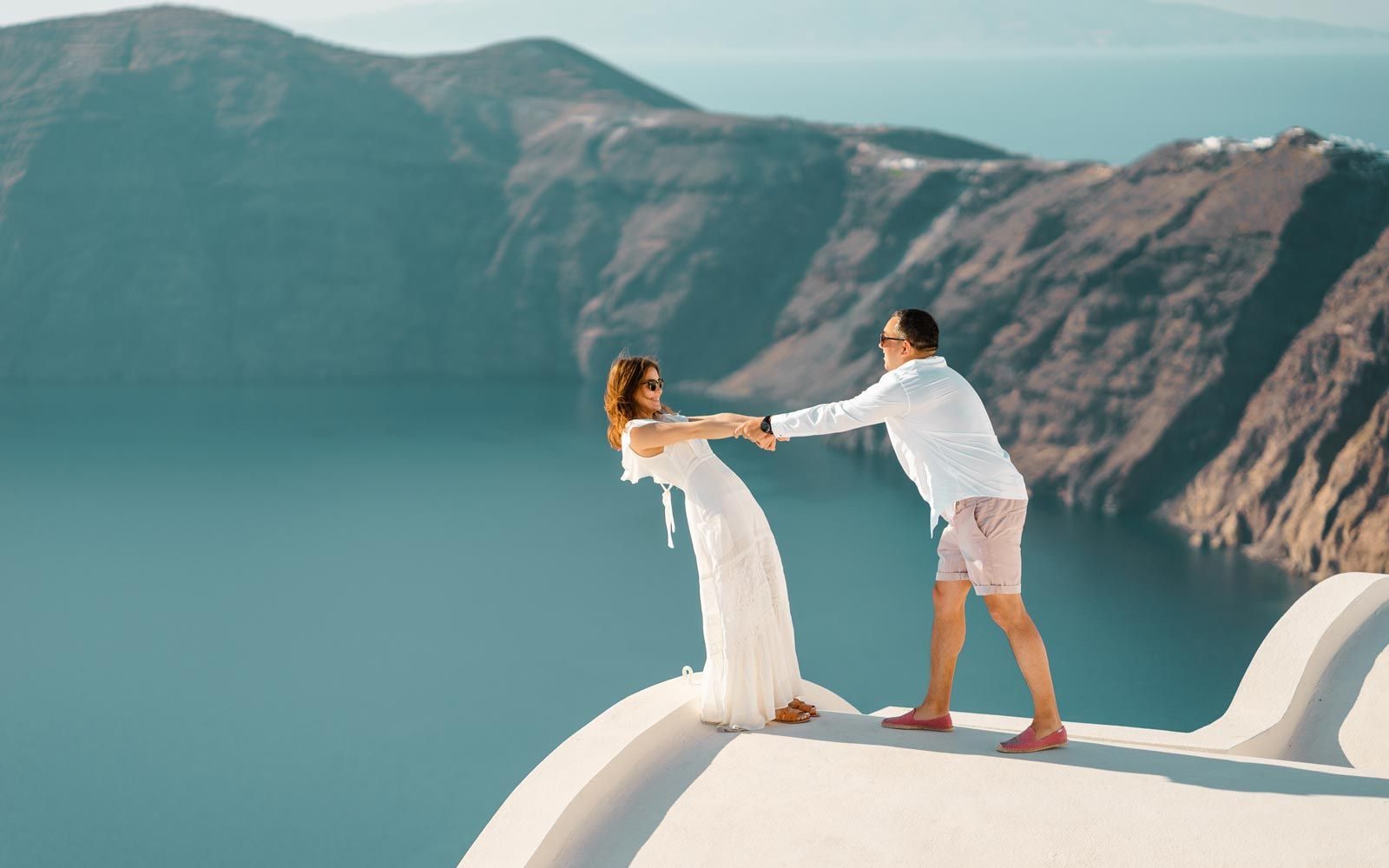 Couple holding hands on a white rooftop above the caldera in Imerovigli
