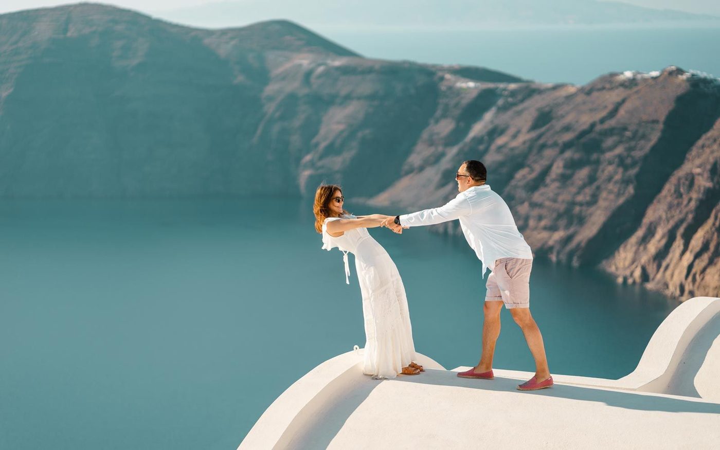 Couple holding hands on a white rooftop above the caldera in Imerovigli