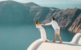 Couple holding hands on a white rooftop above the caldera in Imerovigli