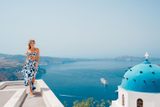 Woman walking along a rooftop ledge in Imerovigli, with the caldera and a cruise ship below
