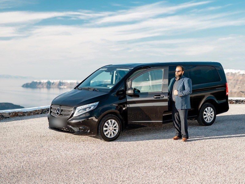 Black Mercedes van and its driver, parked on a gravel lot above the caldera