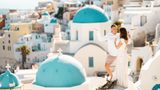 Couple in white with arms raised on a rooftop above the blue domes of Oia