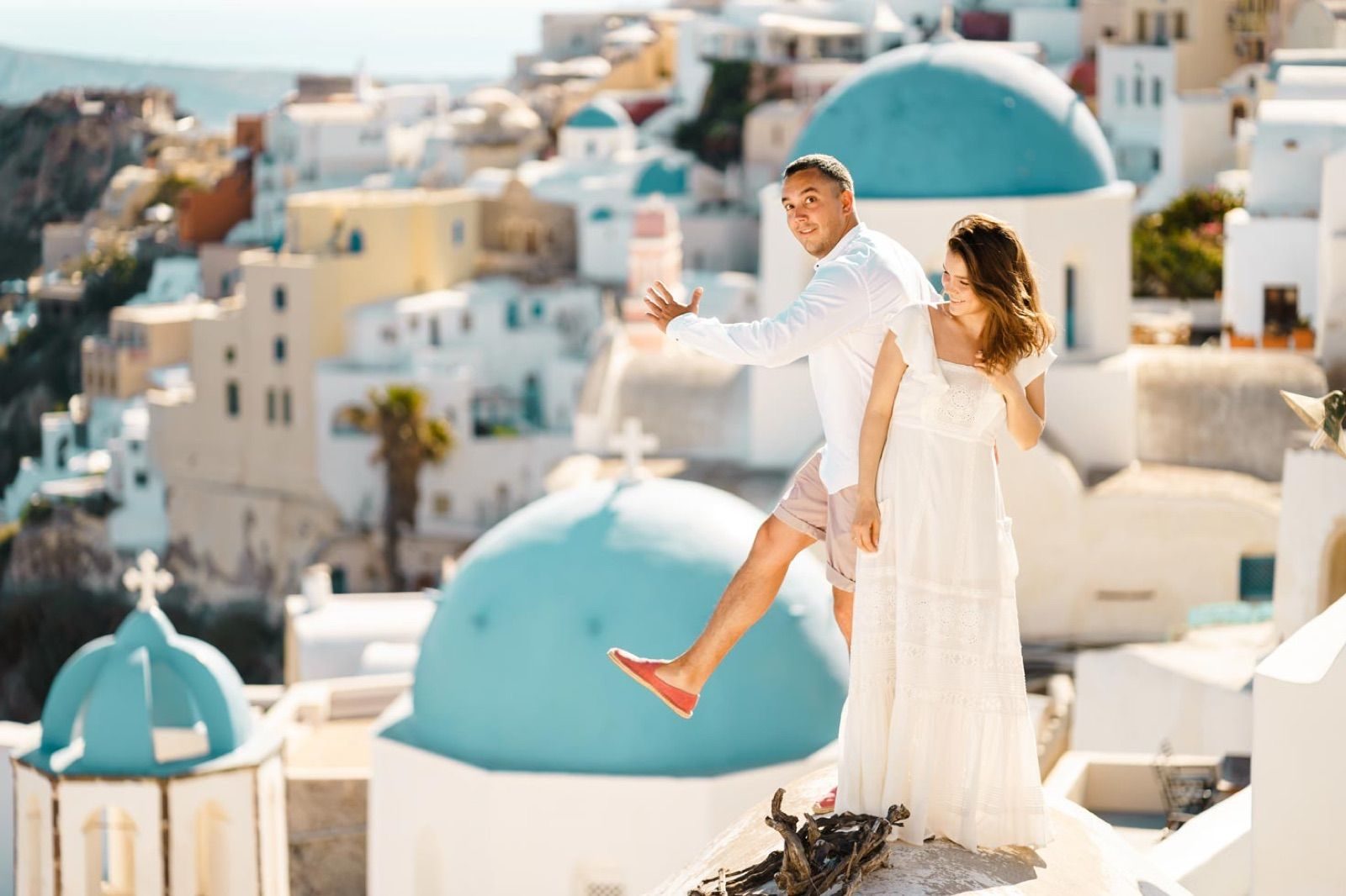 Couple playing for the camera on a rooftop by the blue domes of Oia