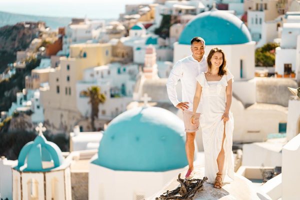 Couple smiling on a rooftop beside the blue domes of Oia