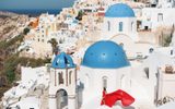 Woman in a red flowing dress beside the blue-domed churches of Oia
