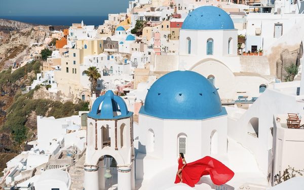 Woman in a red flowing dress beside the blue-domed churches of Oia