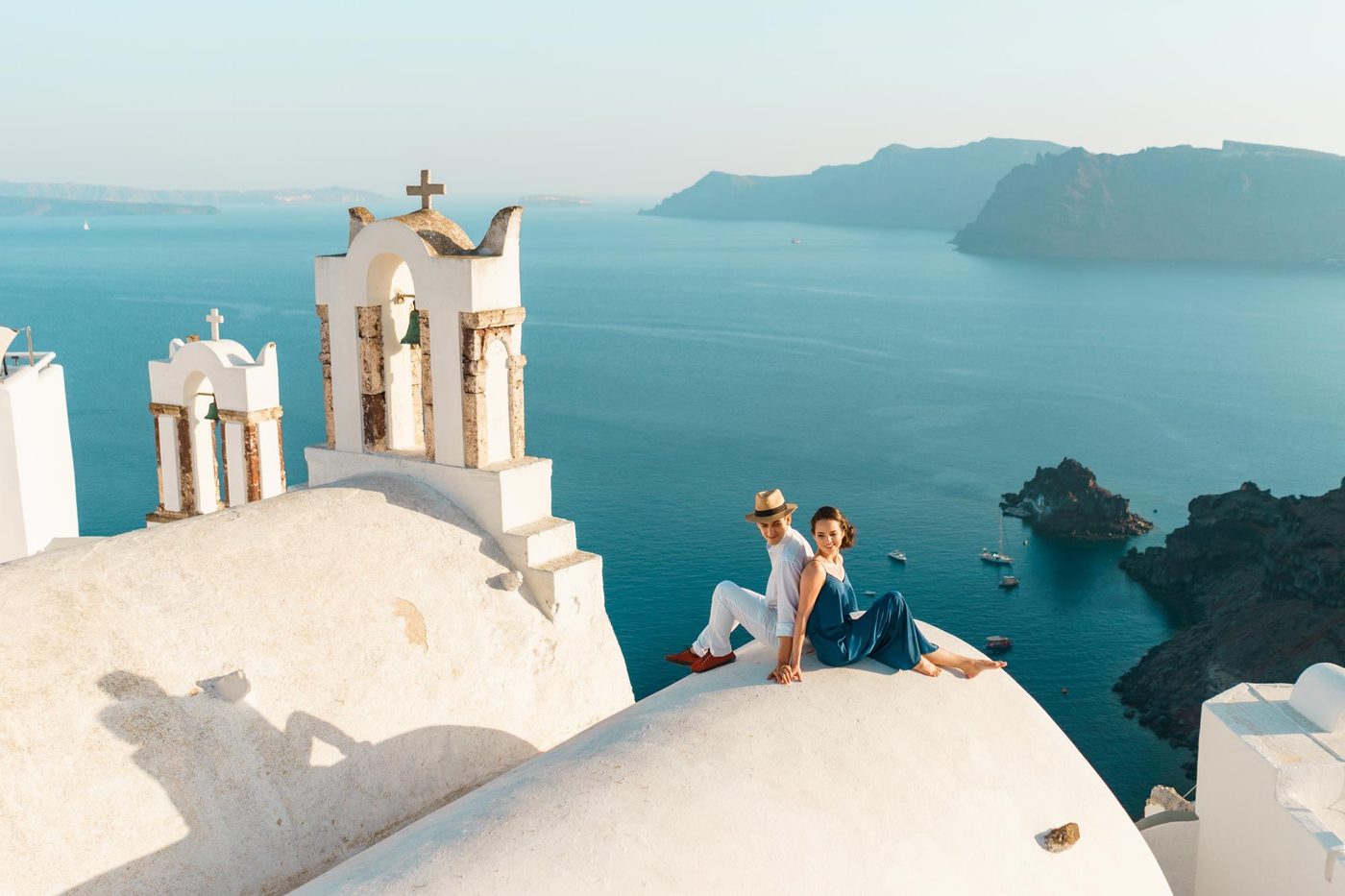 Couple sitting on a whitewashed church roof in Oia, above the Santorini caldera
