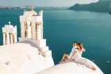 Couple sitting on a white church roof in Oia beside bell towers, looking over the caldera