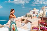 Woman in a floral skirt leaning on a rope railing in Oia, with a windmill behind