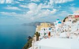 Woman sitting on a whitewashed rooftop in Oia, with blue domes and the caldera behind