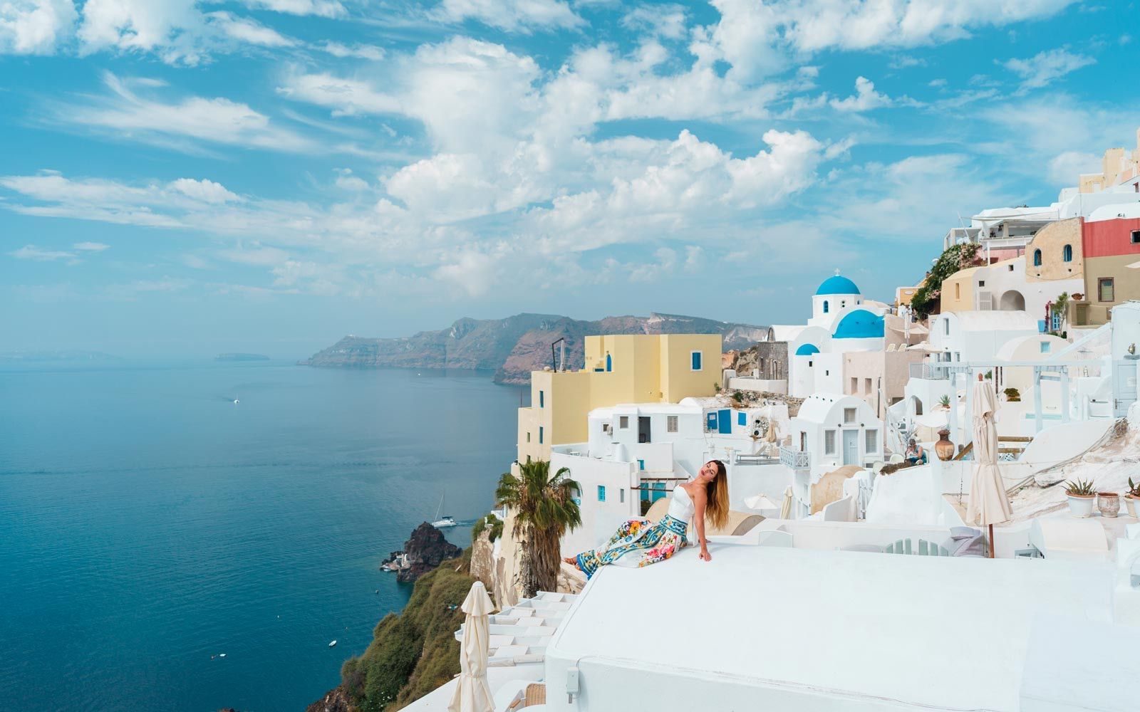 Woman sitting on a whitewashed rooftop in Oia, with blue domes and the caldera behind