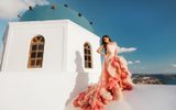 Woman in a pink ruffled gown beside a blue-domed church above the caldera