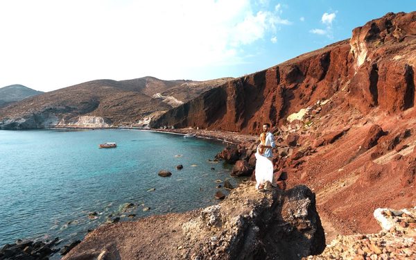 Couple on the rocks at Red Beach, below red cliffs beside a turquoise cove