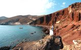 Couple on the rocks at Red Beach, below red cliffs beside a turquoise cove