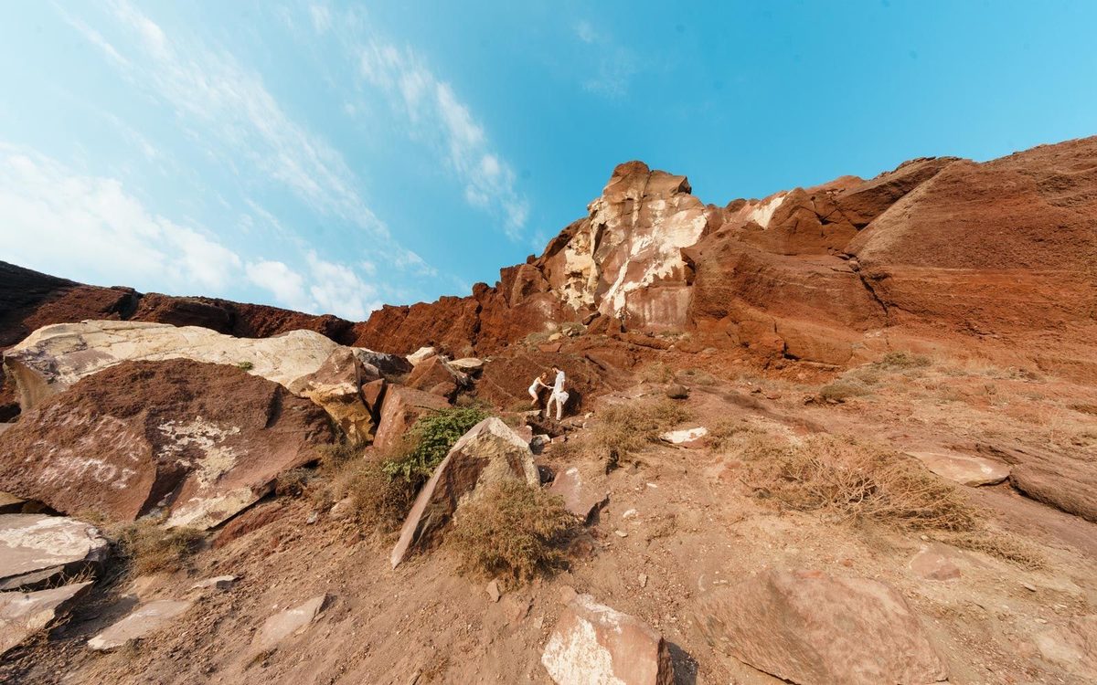 Red volcanic cliffs and boulders at Red Beach, with two people climbing the rocks