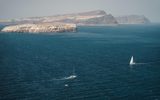 Sailboats on deep blue sea below pale island cliffs, seen from the lighthouse