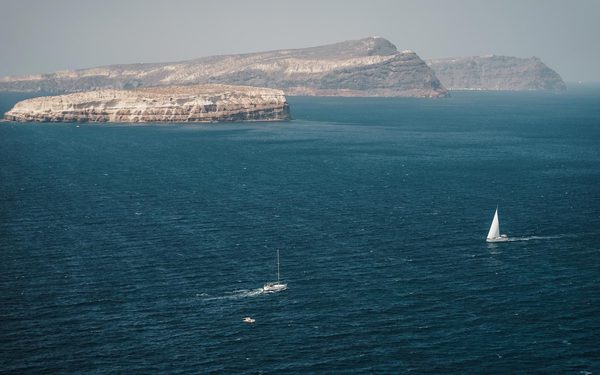Sailboats on deep blue sea below pale island cliffs, seen from the lighthouse