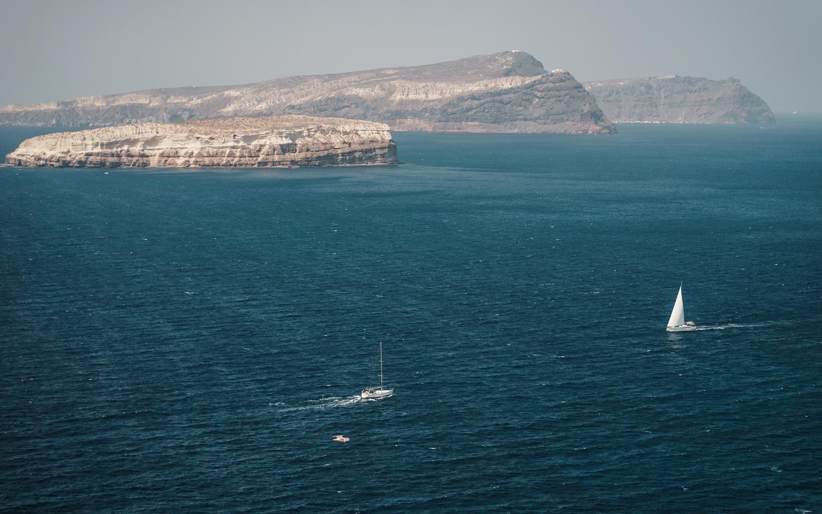 Sailboats on deep blue sea below pale island cliffs, seen from the lighthouse