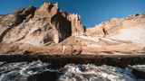 Couple hand in hand on a black volcanic beach, surf in front and eroded white cliffs behind