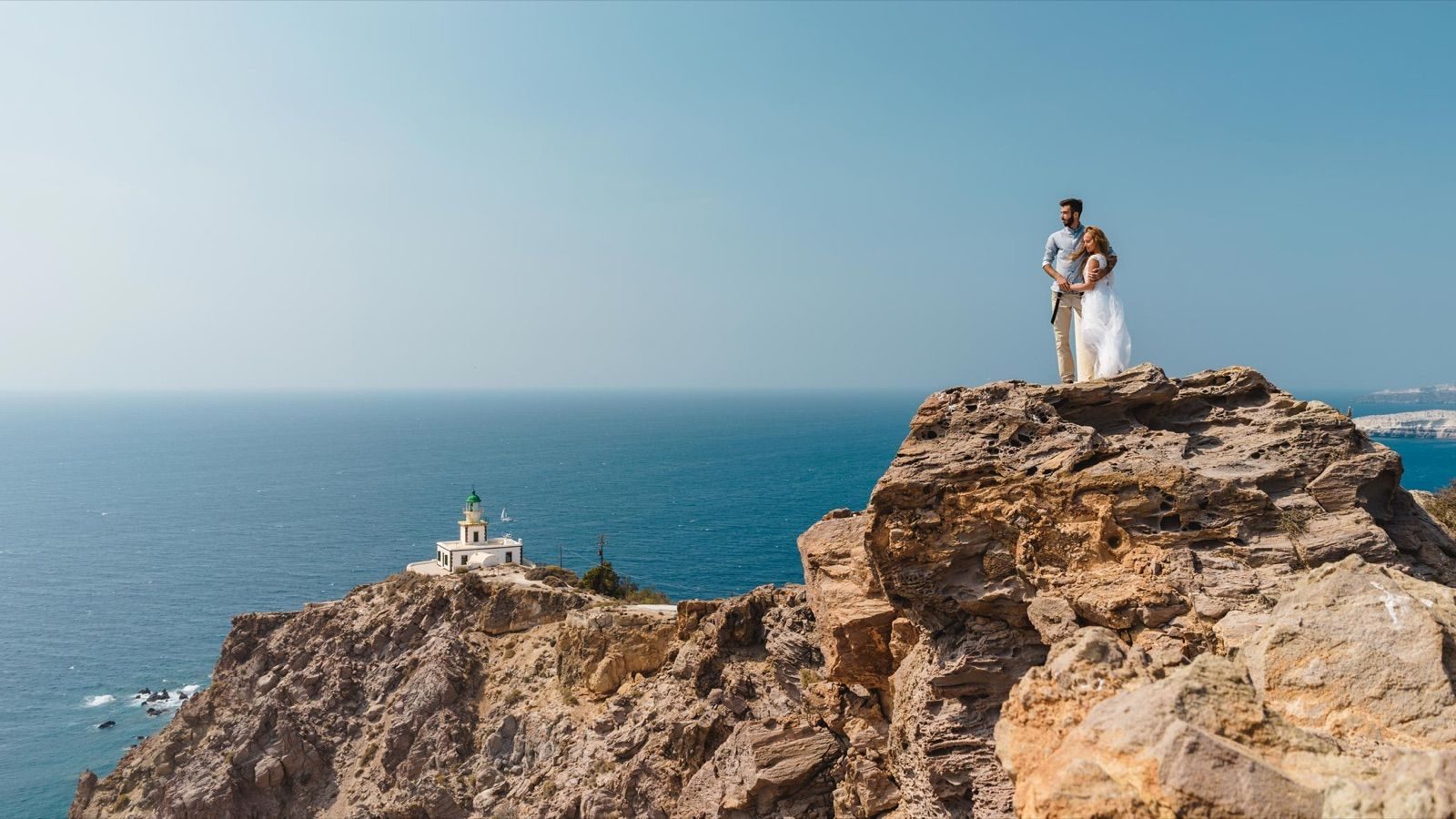 Couple standing on a rocky headland above the lighthouse, with open sea beyond