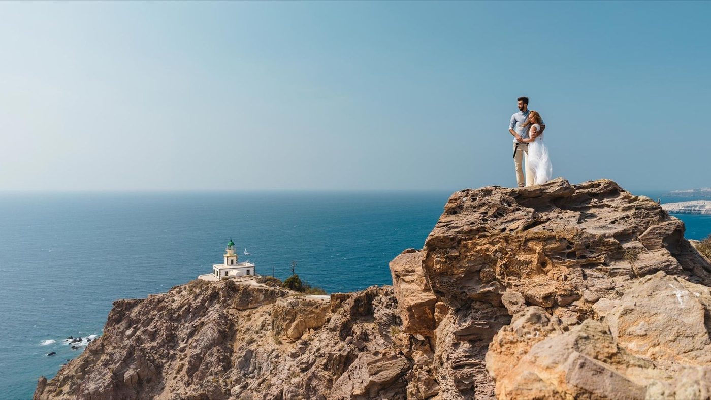 Couple standing on a rocky headland above the lighthouse, with open sea beyond