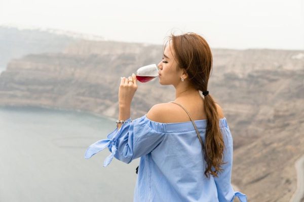 Woman drinking red wine above the caldera cliffs in Santorini