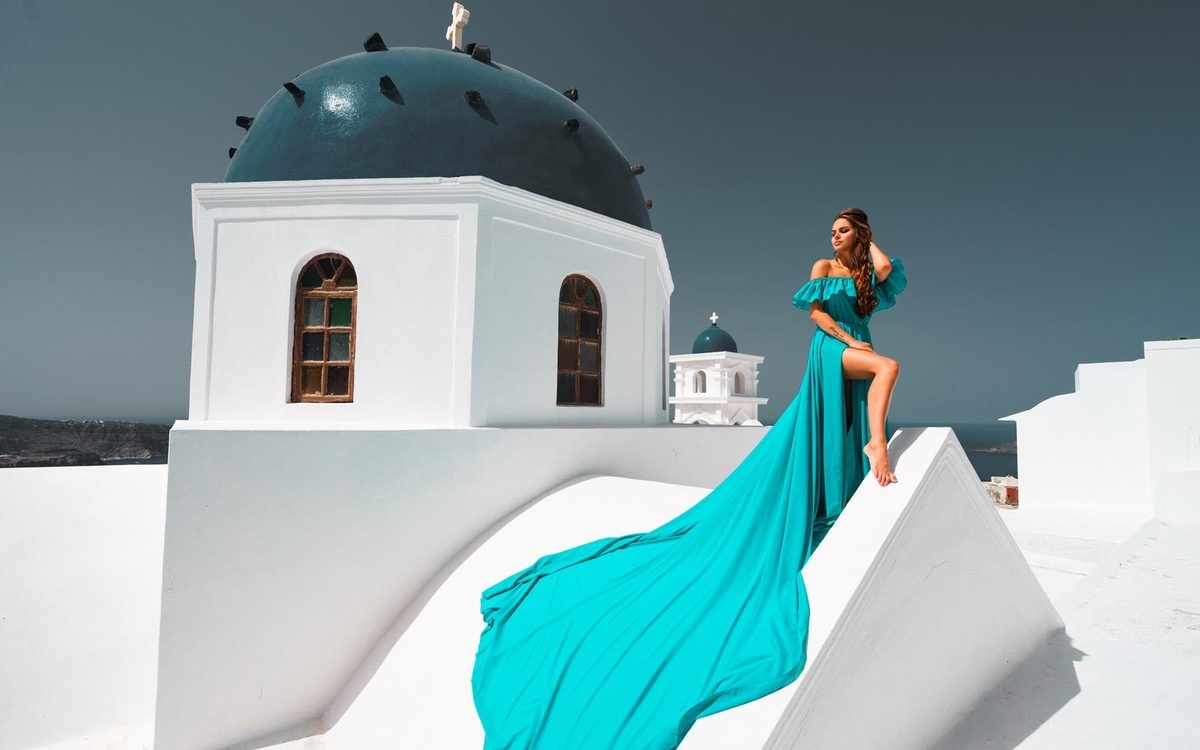 Woman in a long turquoise dress seated on a church roof beside a blue dome
