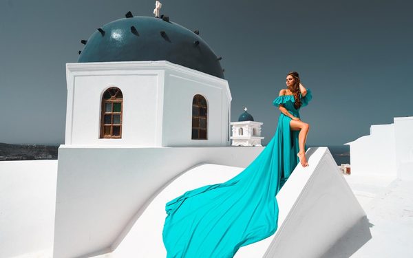 Woman in a long turquoise dress seated on a church roof beside a blue dome