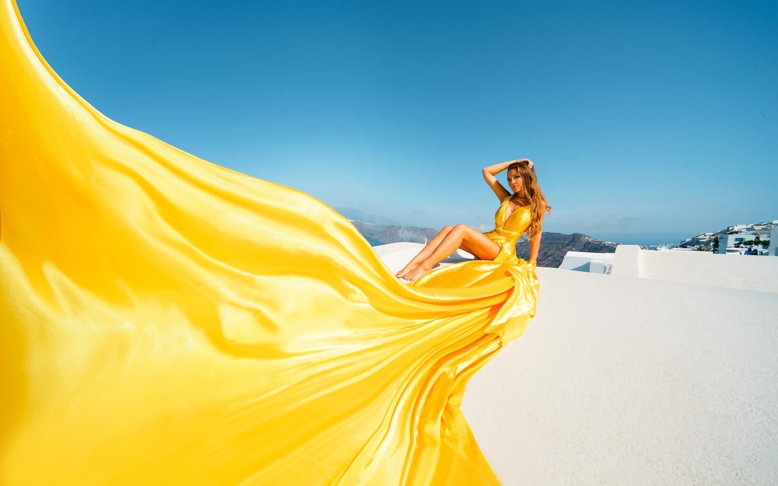 Woman in a yellow flying dress seated on a white rooftop in Santorini