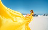 Woman in a yellow flying dress seated on a white rooftop in Santorini
